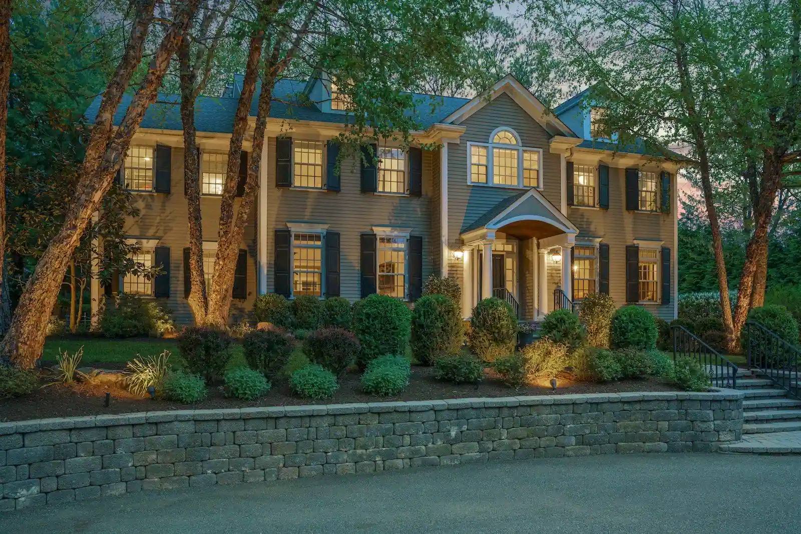 Stately New Jersey colonial residence glowing at twilight behind landscaped gardens